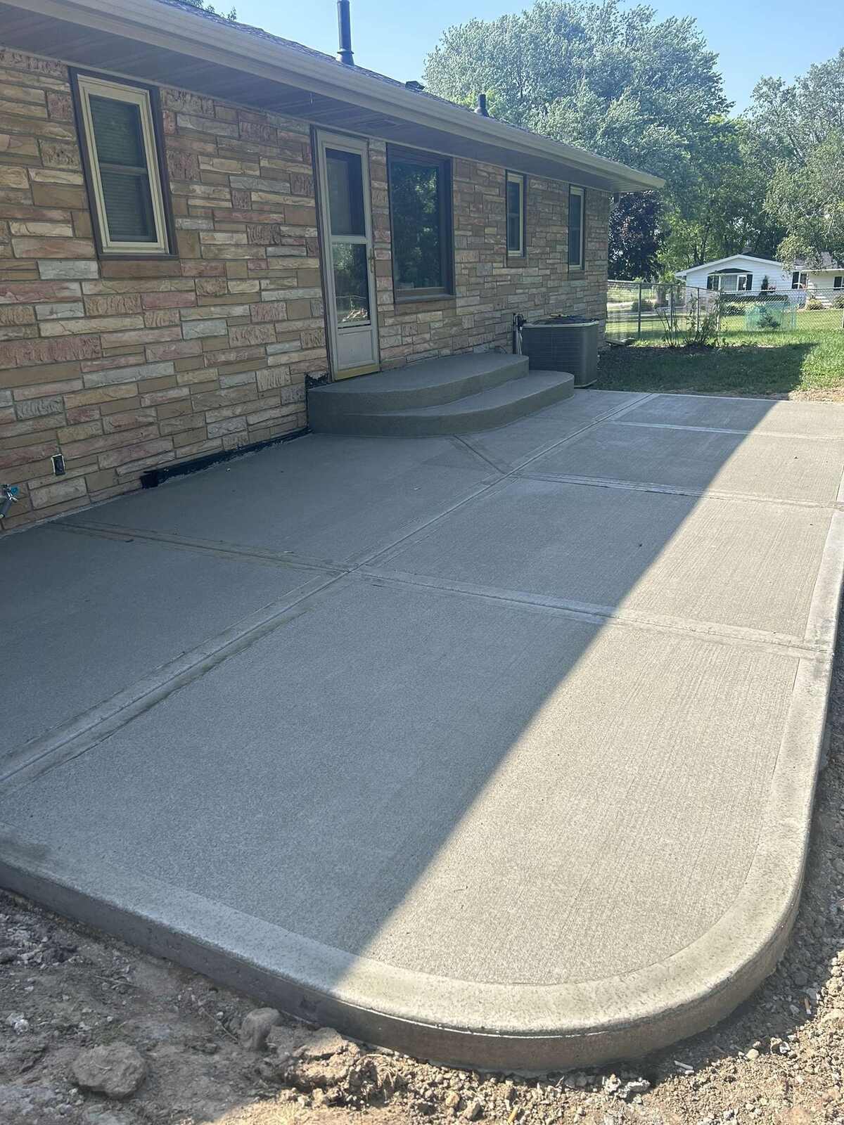 New concrete patio with rounded corner and steps behind a stone ranch house