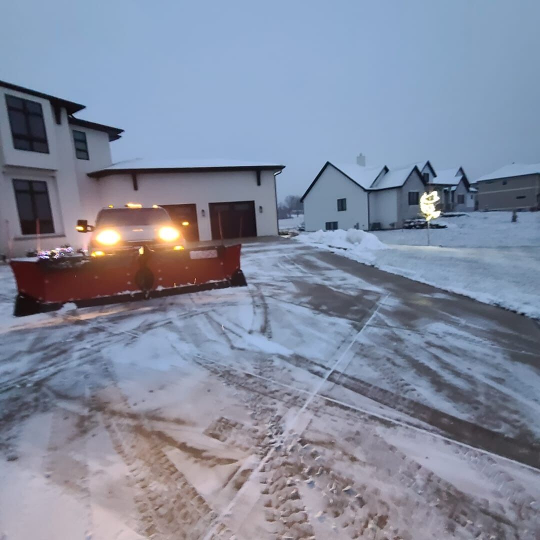 Pickup truck with a snow plow clearing a residential driveway at dusk