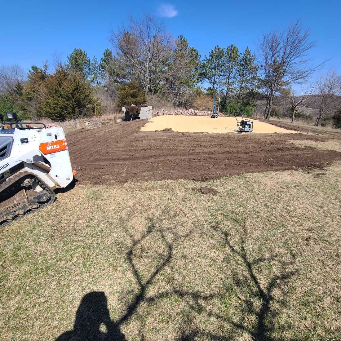 Compact track loader beside graded soil and a compacted gravel pad